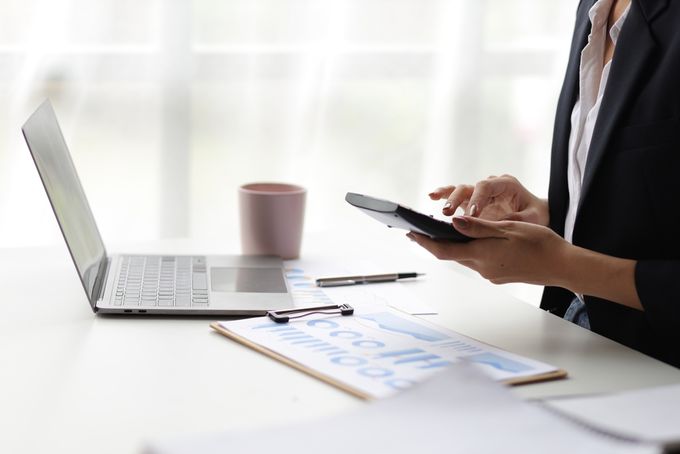Woman sitting in front of a laptop while working on a calculator and checking  data on a spreadsheet