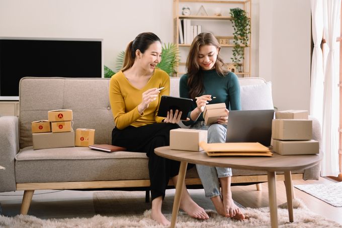 Two young professionals sitting on a couch while preparing boxes for shipping
