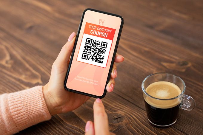 Close-up of a cell phone in a female person's hand with the screen showing a discount coupon next to a coffee cup