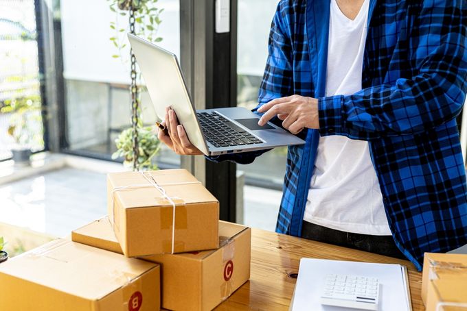 Man holding laptop with boxes and documents on the table in front of him