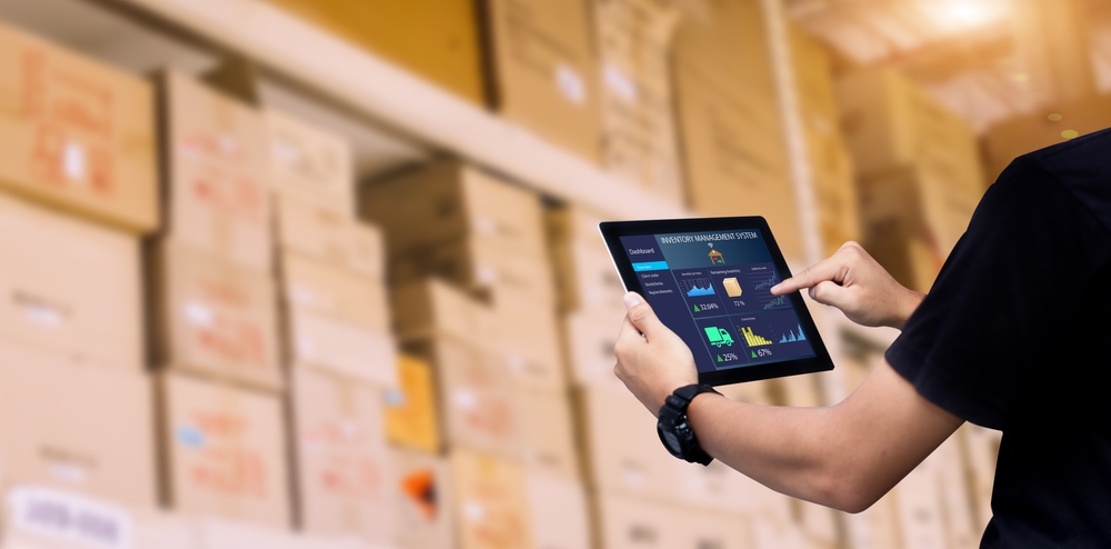 Man holding an iPad navigating an inventory sync app in front of boxes of products